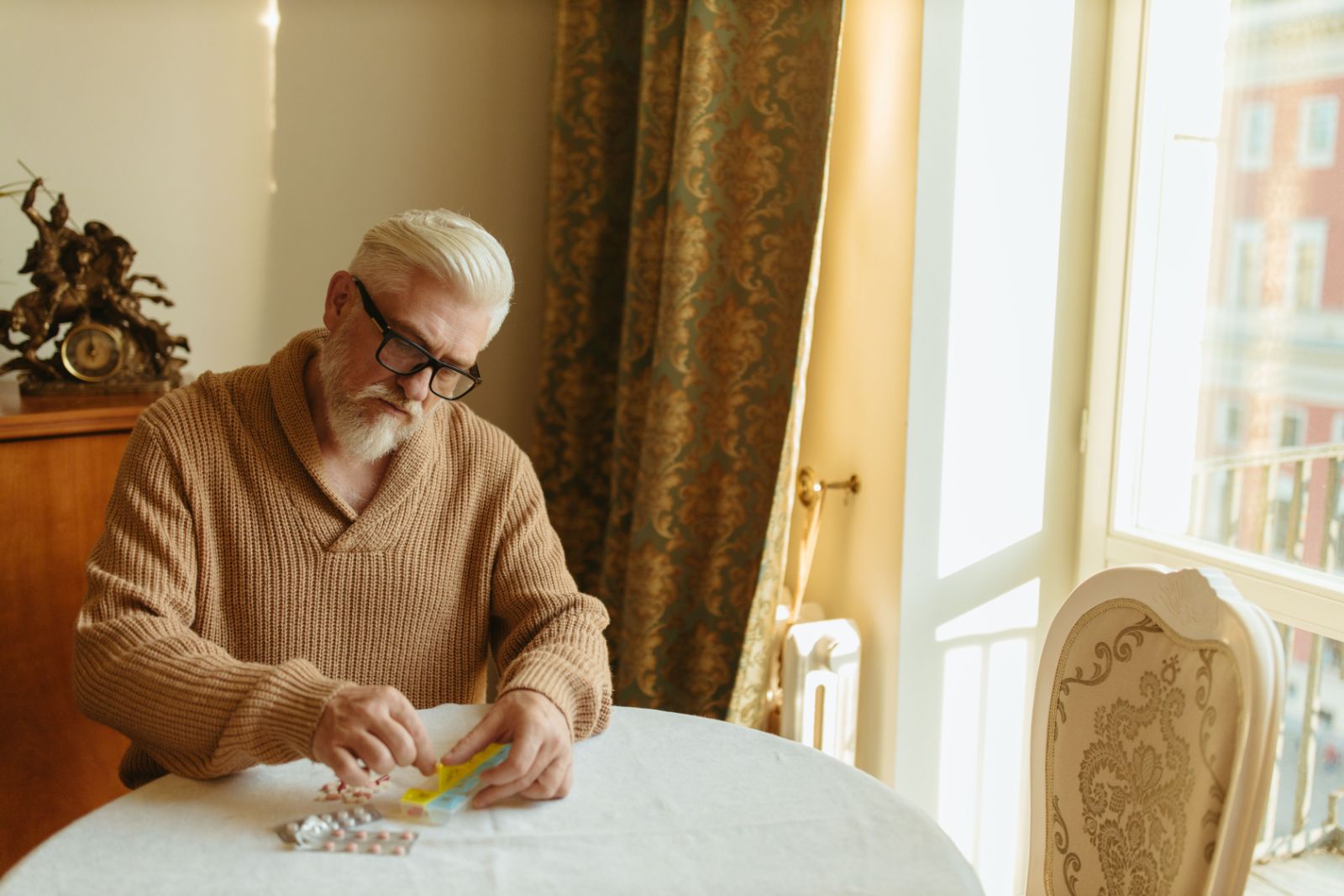 Hombre mayor organizando sus pastillas en la mesa del salón