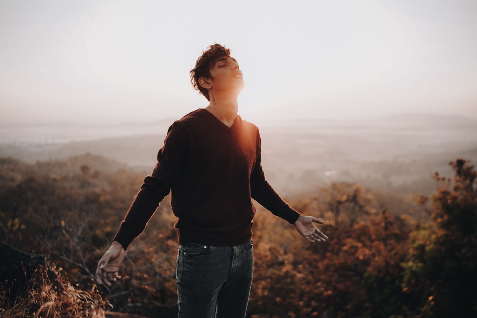Hombre con los brazos abiertos al amanecer en una colina con niebla